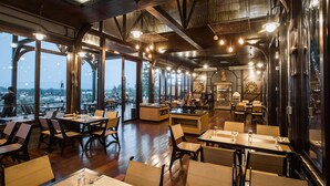Un restaurante con mesas y sillas de madera, ventanas amplias y lámparas colgantes.