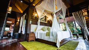 Un dormitorio amplio con cama con dosel, suelo de madera y vistas al exterior.