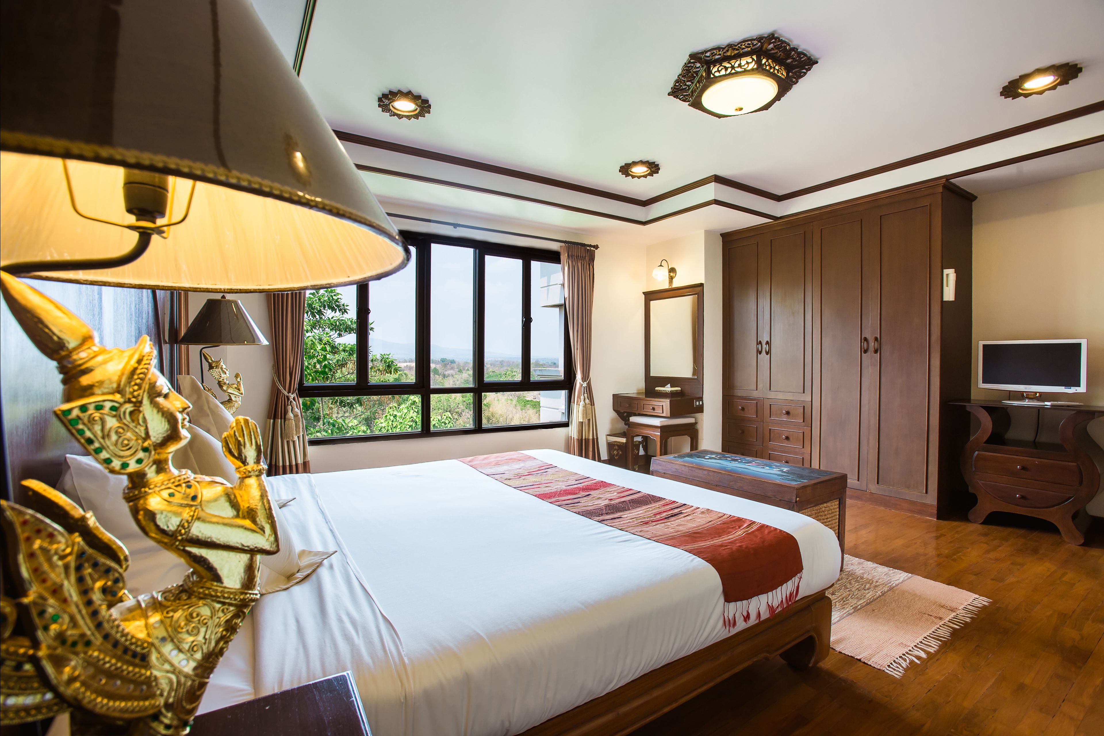A hotel room with a large bed, a desk, a wardrobe, and a television.