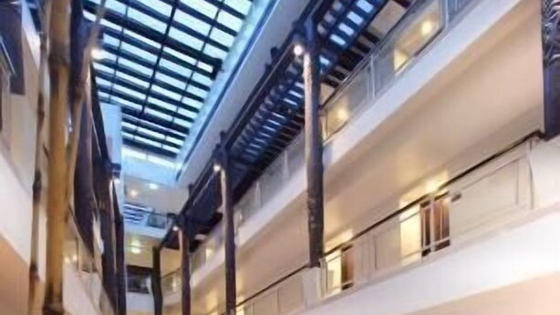 Un hall d’hôtel à plusieurs niveaux, doté d’une verrière, de plusieurs espaces de restauration et d’un espace salon central.