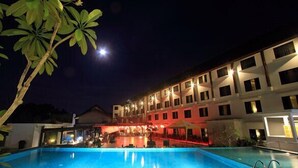 Vue nocturne d’un hôtel doté d’une piscine, illuminée par un éclairage artificiel.