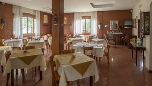 A spacious dining area with multiple tables and chairs, large windows with curtains, and a brick wall. - Hotel Santorotto (Sinalunga)