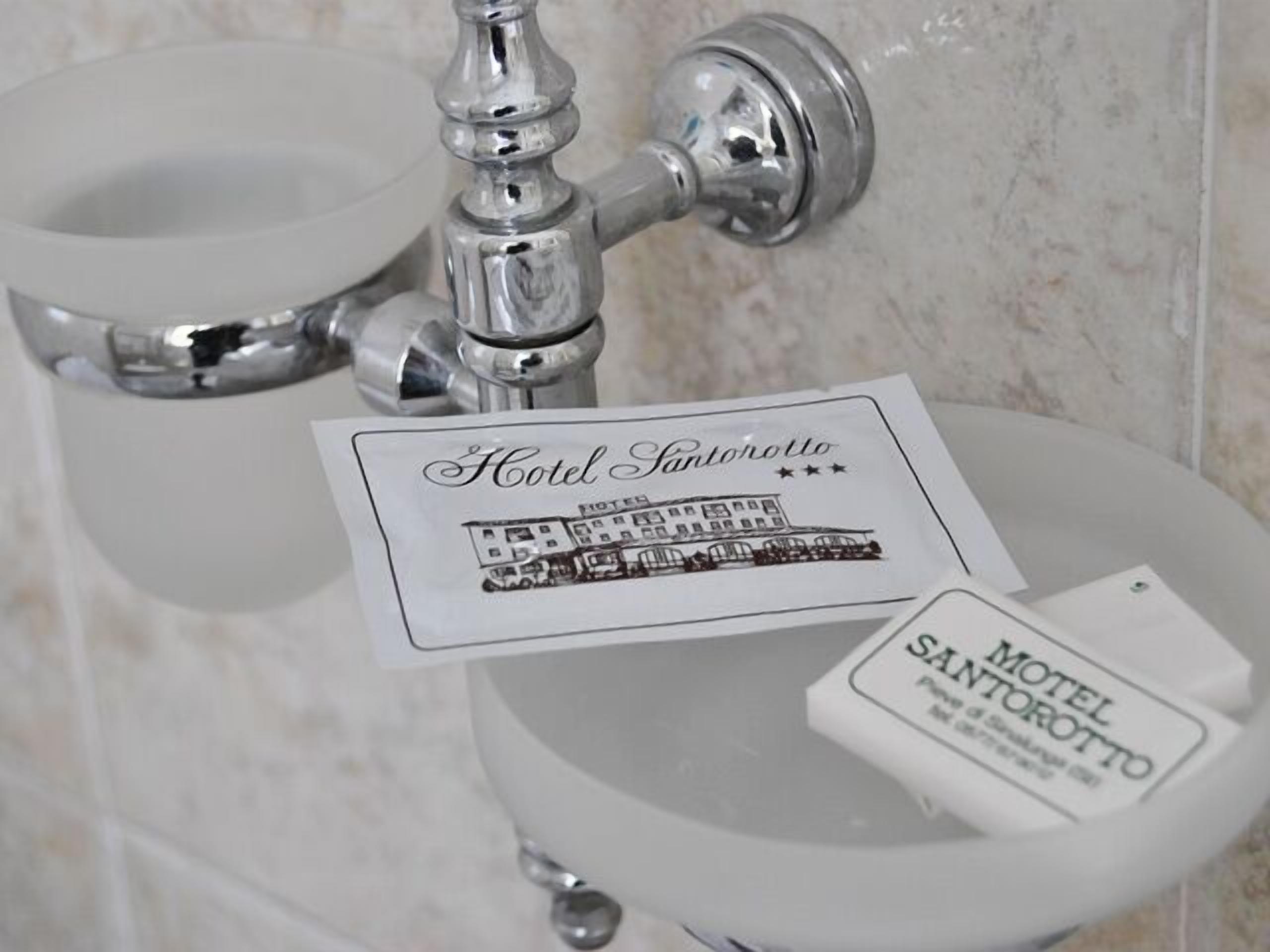 A bathroom sink with a paper towel holder and a card labeled "Hotel Santorotto."