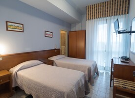 Habitación de hotel con dos camas, un armario de madera, un escritorio con una silla y una ventana con cortinas.