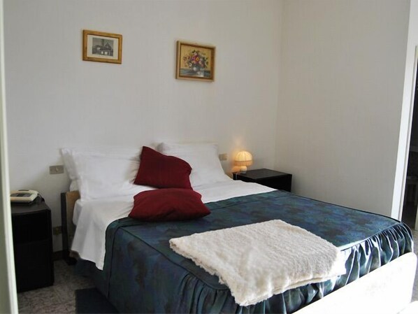 A neatly made bed with a blue cover, two red pillows, and a white throw blanket. There are two framed pictures on the wall above the bed.