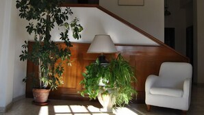 A room with a wooden reception desk, a white armchair, and two potted plants. - Hotel Santorotto (Sinalunga)