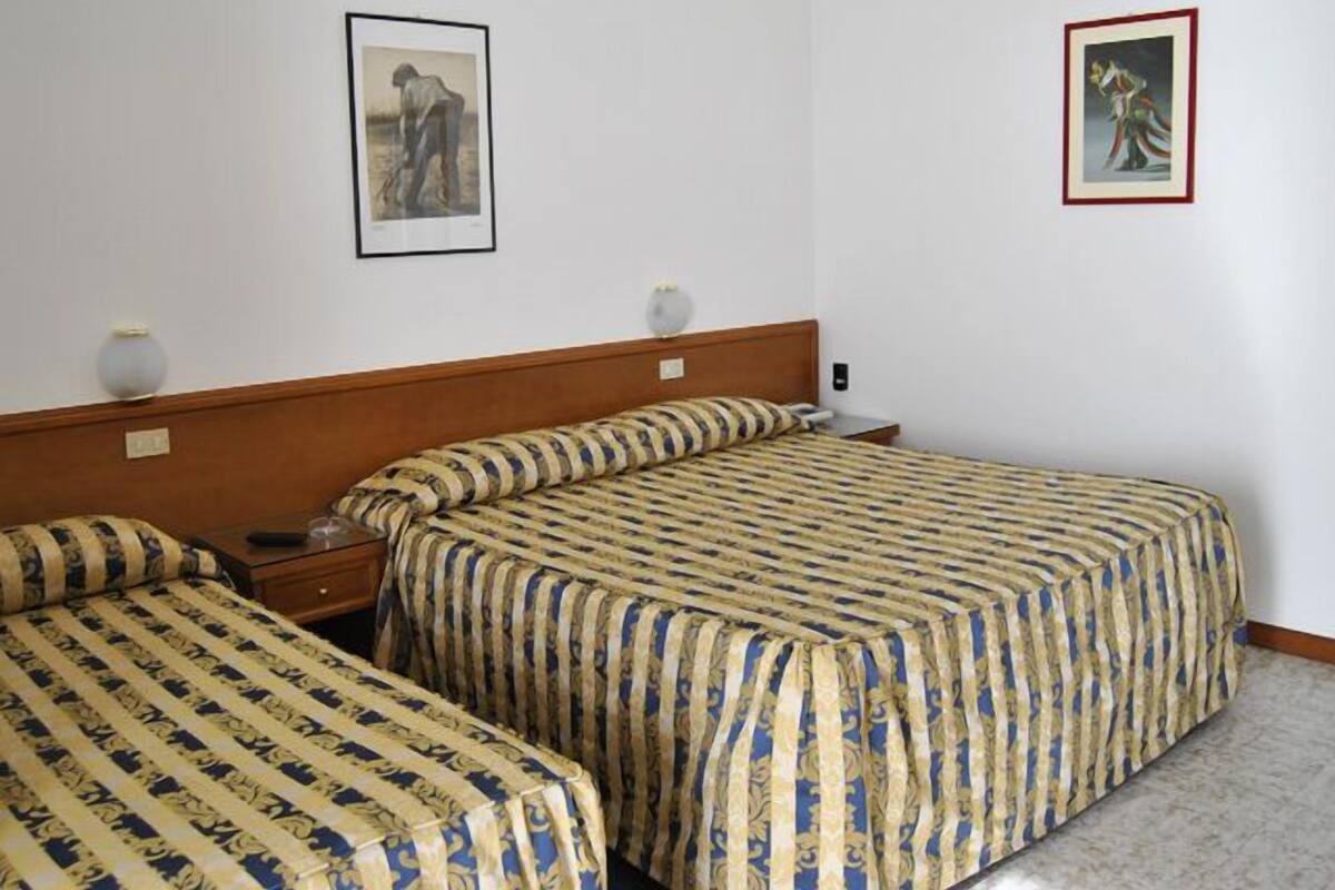 Ein Hotelzimmer mit zwei Betten, einem Holzkopfstück, einem Nachttisch, einer Lampe und zwei gerahmten Bildern an der Wand.
