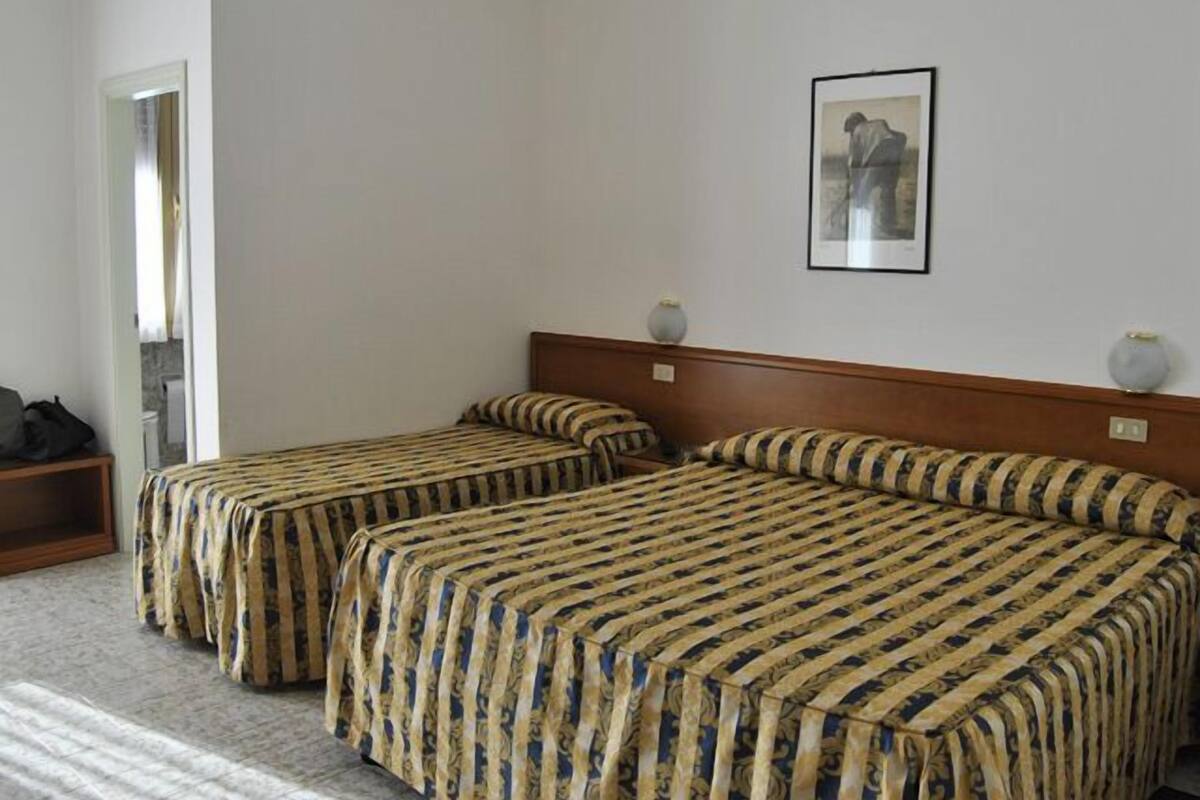 Ein Hotelzimmer mit zwei Einzelbetten, einem Holzkopfstück, einem gerahmten Bild an der Wand und einem kleinen Tisch mit einer Vase.