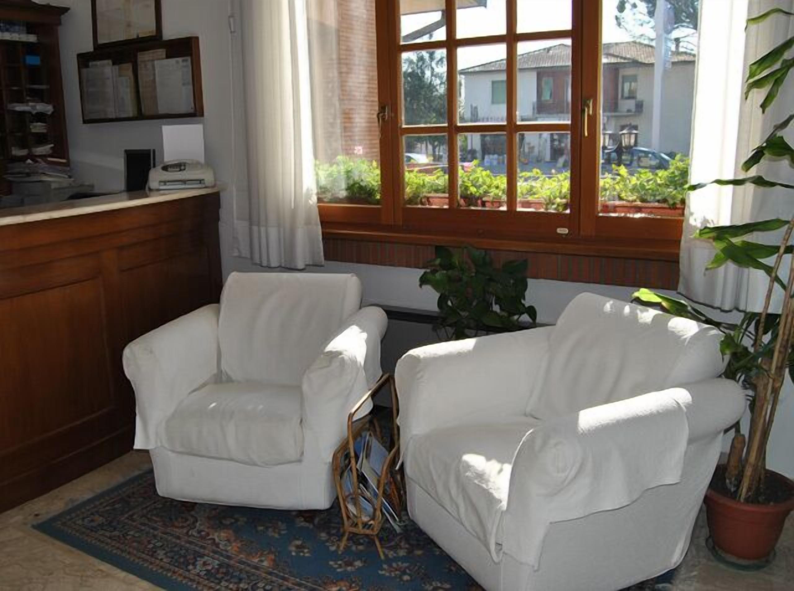 Una habitación con dos sillones blancos, un escritorio de madera, un ventanal con vistas al exterior y una planta en maceta.