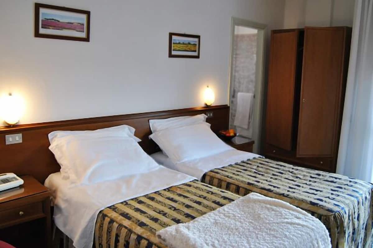 Ein Hotelzimmer mit zwei Betten, einem Kleiderschrank und zwei Wandlampen.