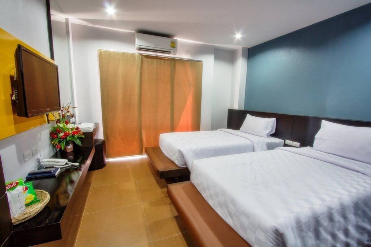 Ein Hotelzimmer mit zwei Betten, einem Schreibtisch mit Telefon und Korb, einem an der Wand befestigten Fernseher und einer Klimaanlage.