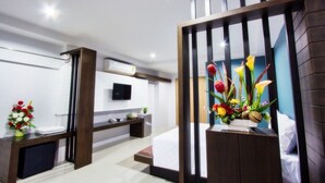 Quarto de hotel moderno com cama, escrivaninha, televisão e um arranjo floral decorativo.