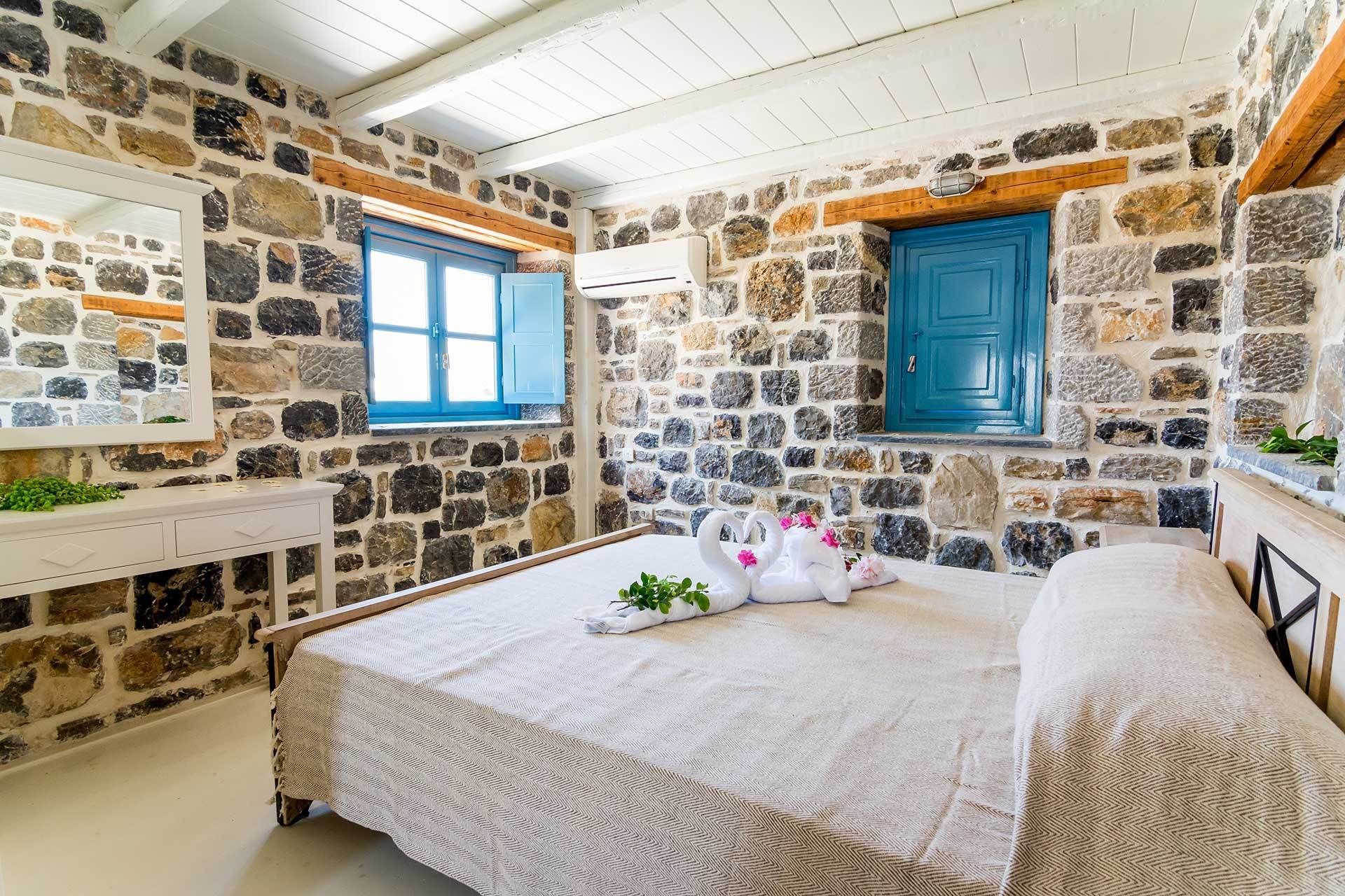A stone-walled room with a bed, two windows, and a white dresser.