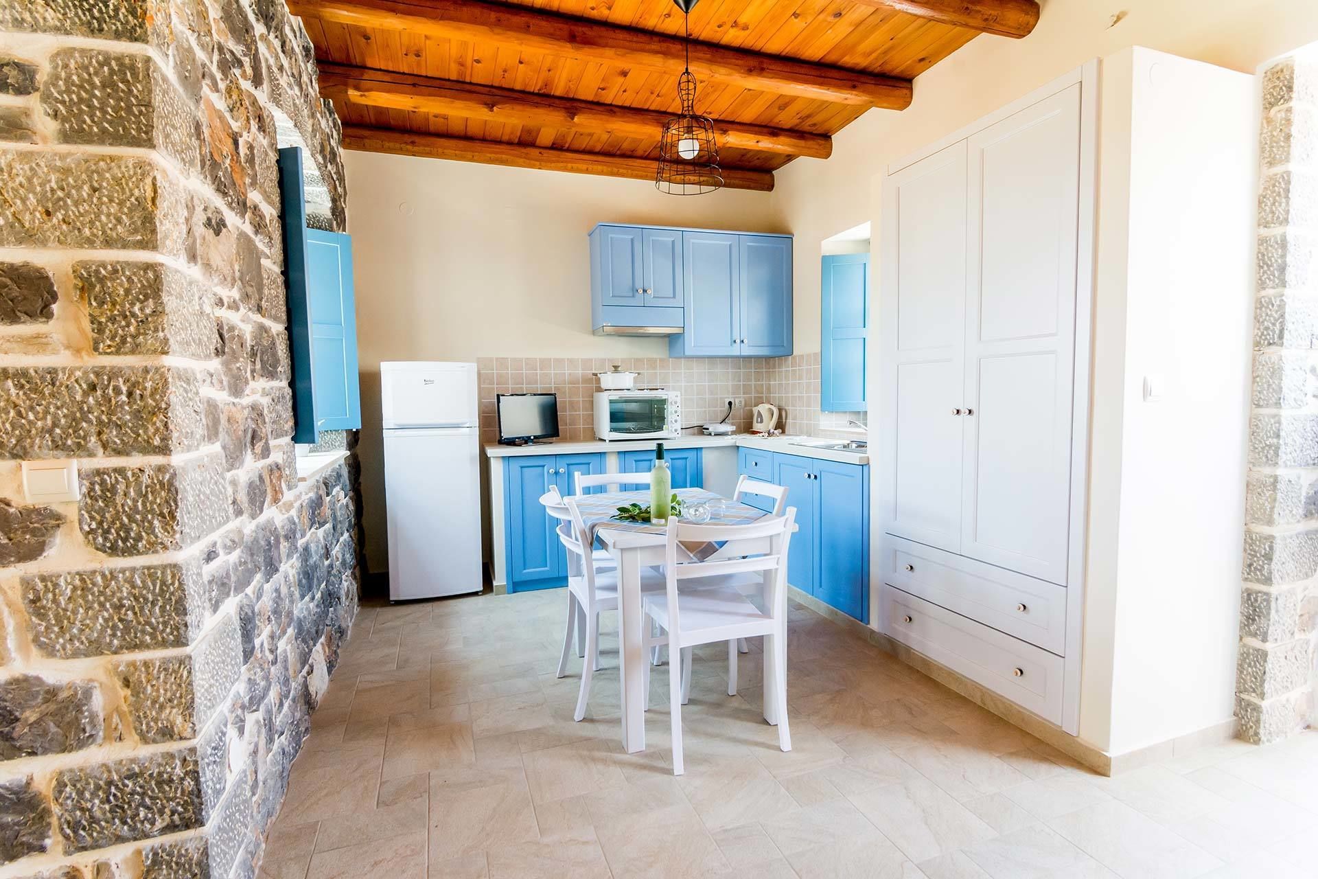 Una cocina compacta con armarios azules, un refrigerador blanco, un microondas y una mesa de comedor con sillas.