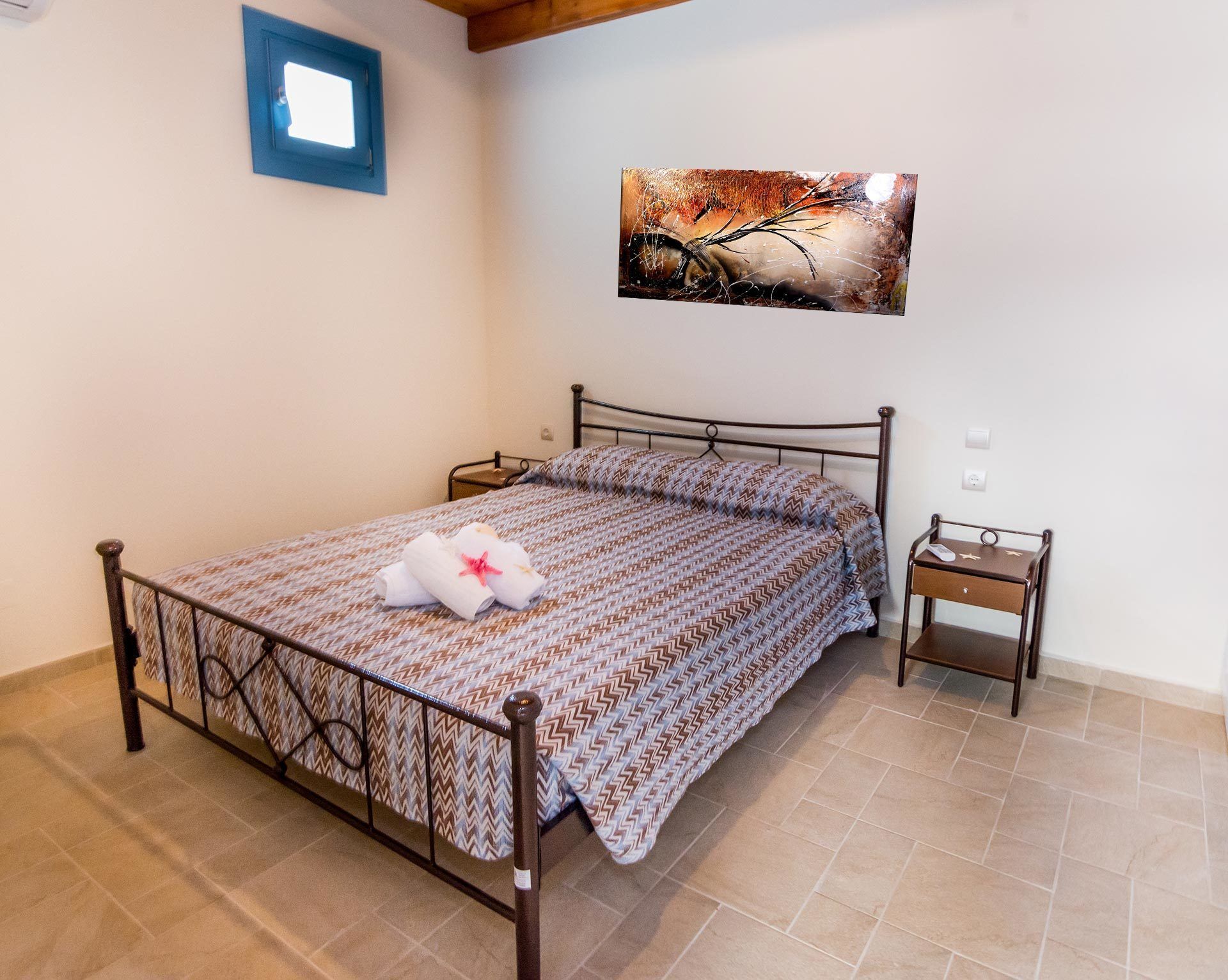 A neatly made bed with a patterned bedspread and a decorative pillow, a bedside table with a lamp, and a wall-mounted picture.