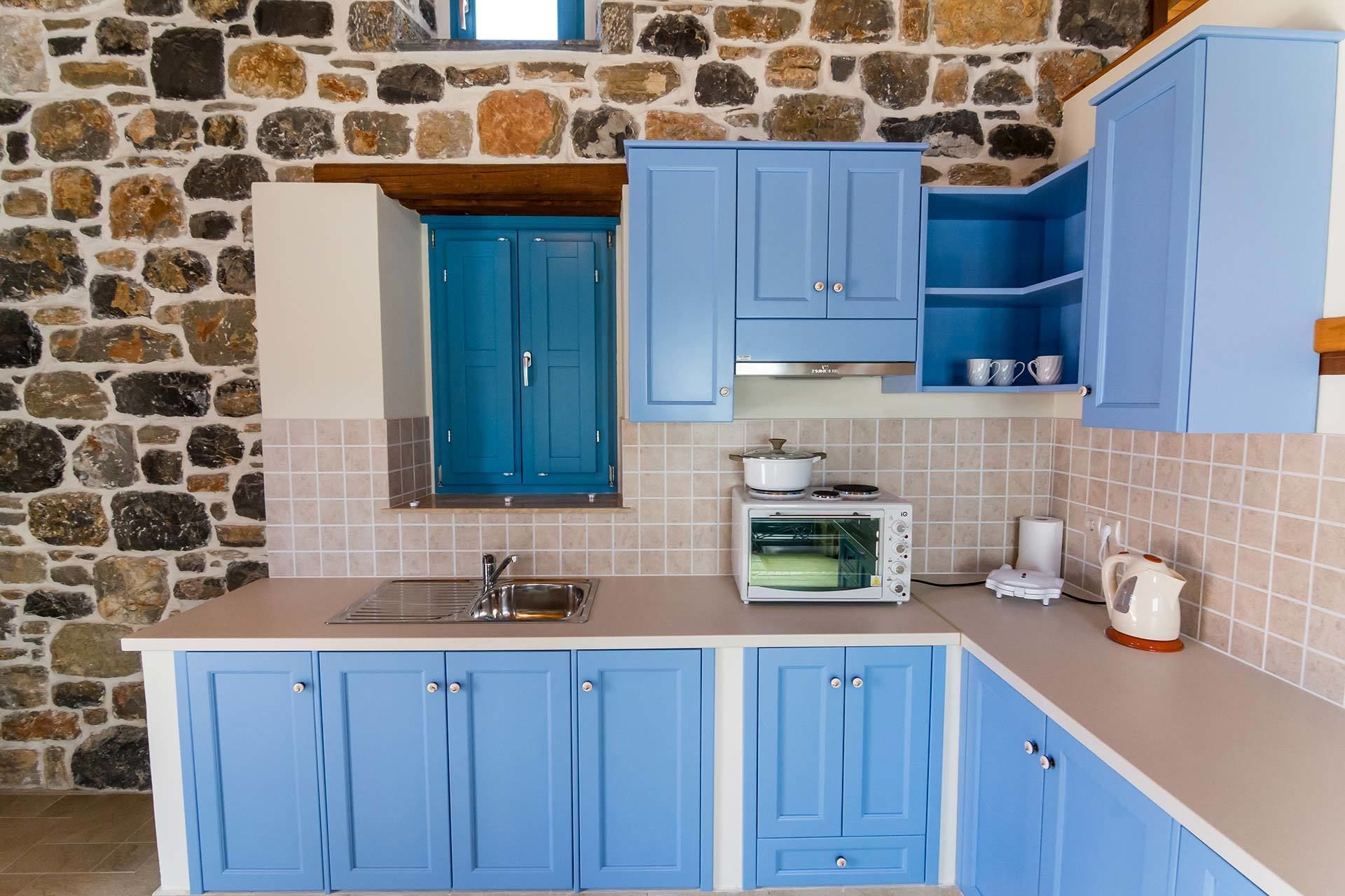 A kitchen with blue cabinets, a stone wall, a microwave, and a sink.