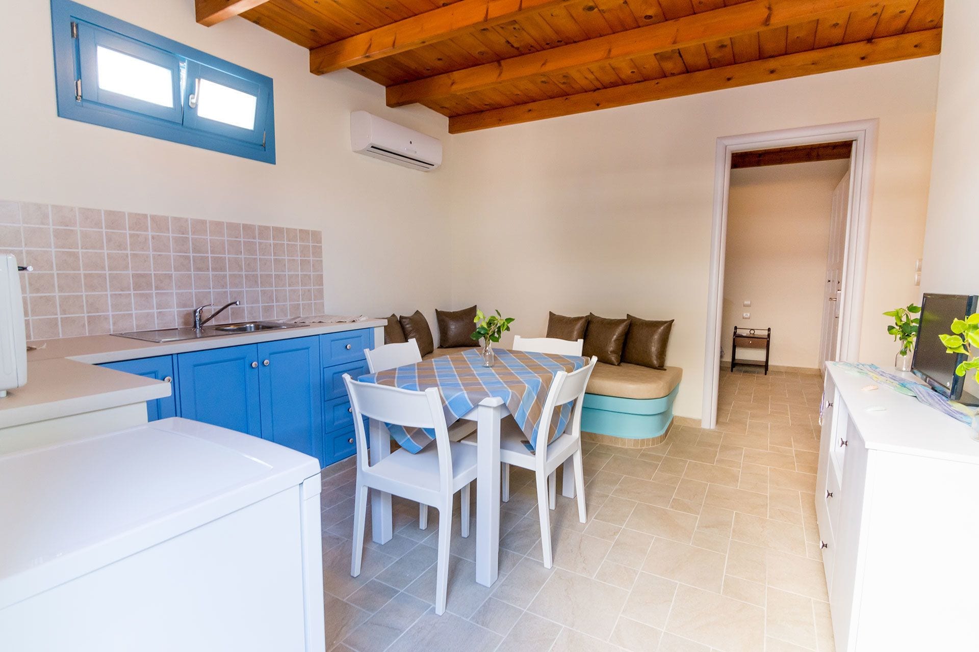 A compact kitchen with blue cabinets, a dining area with a table and chairs, and a wooden ceiling.