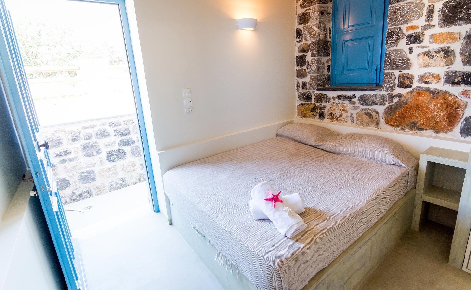 A bedroom with a stone wall, a blue door, and a bed with a towel and starfish decoration.