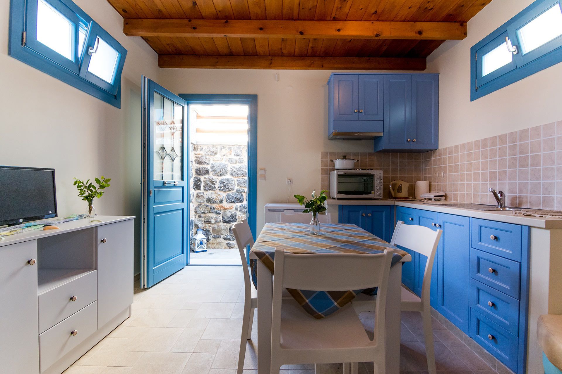 Een keuken met blauwe kastjes, een stenen muur, een magnetron en een eethoek met een tafel en stoelen.