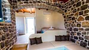 A cozy room with a stone wall, a sofa with cushions, a bed, and a staircase leading to another area.