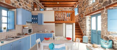 A spacious kitchen with blue cabinets, a dining area with a striped tablecloth, and a stone wall.