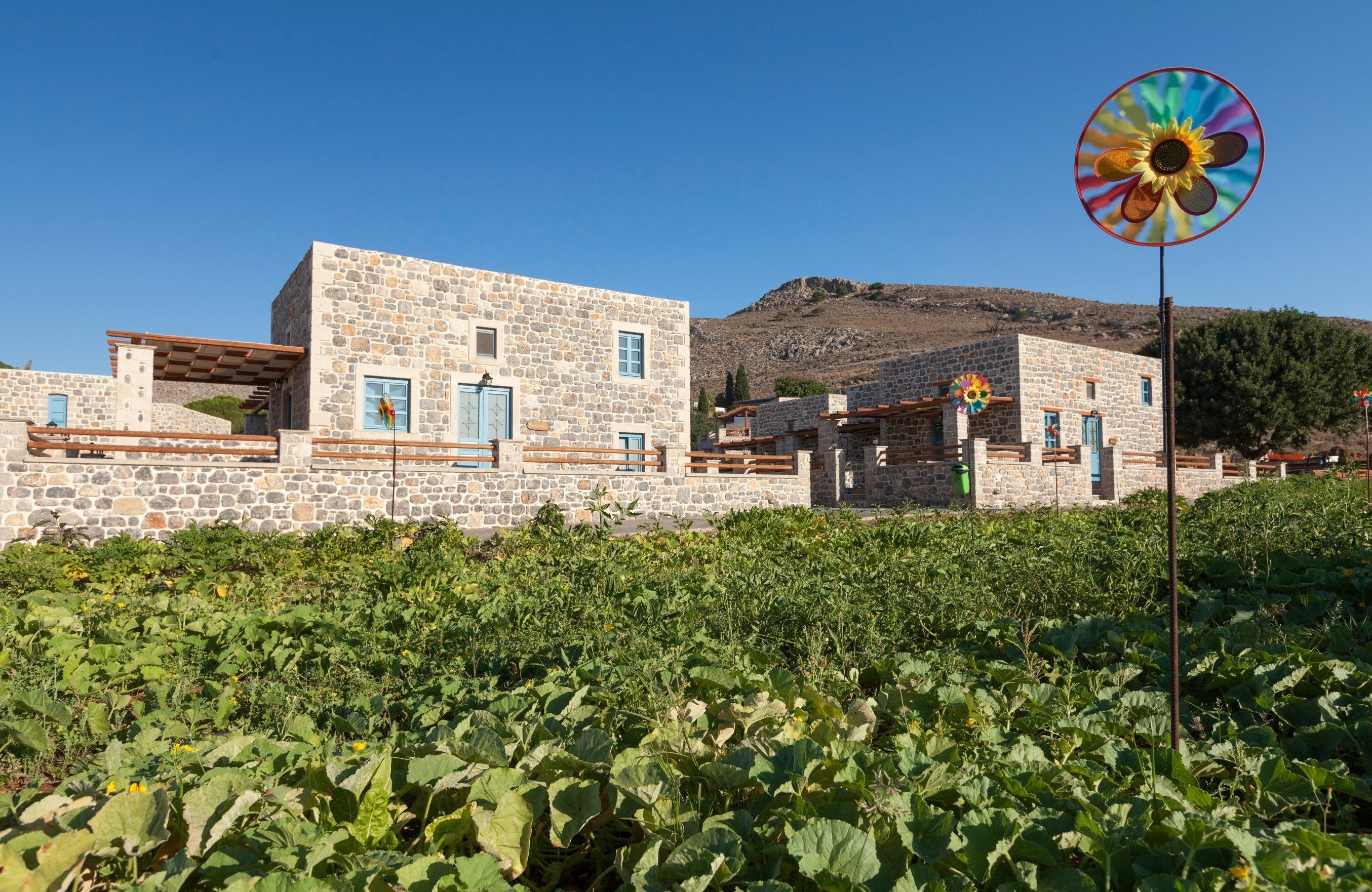 Un edificio de piedra con techo plano y un gran molino de viento con forma de flor en primer plano.