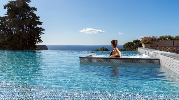 Una persona en un jacuzzi con vistas al océano y una piscina con azulejos.