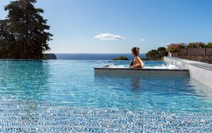 Una persona en un jacuzzi con vistas al océano y una piscina con azulejos.