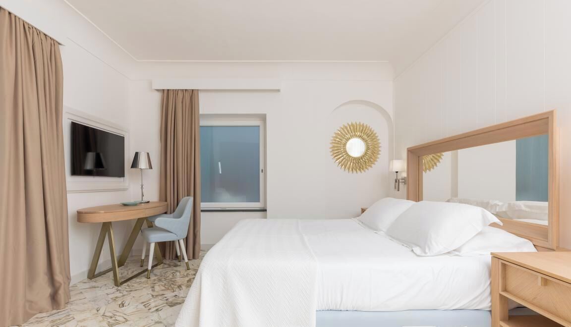 Ein Hotelzimmer mit Bett, Schreibtisch, Stuhl, Fernseher und einem Fenster mit Vorhängen.