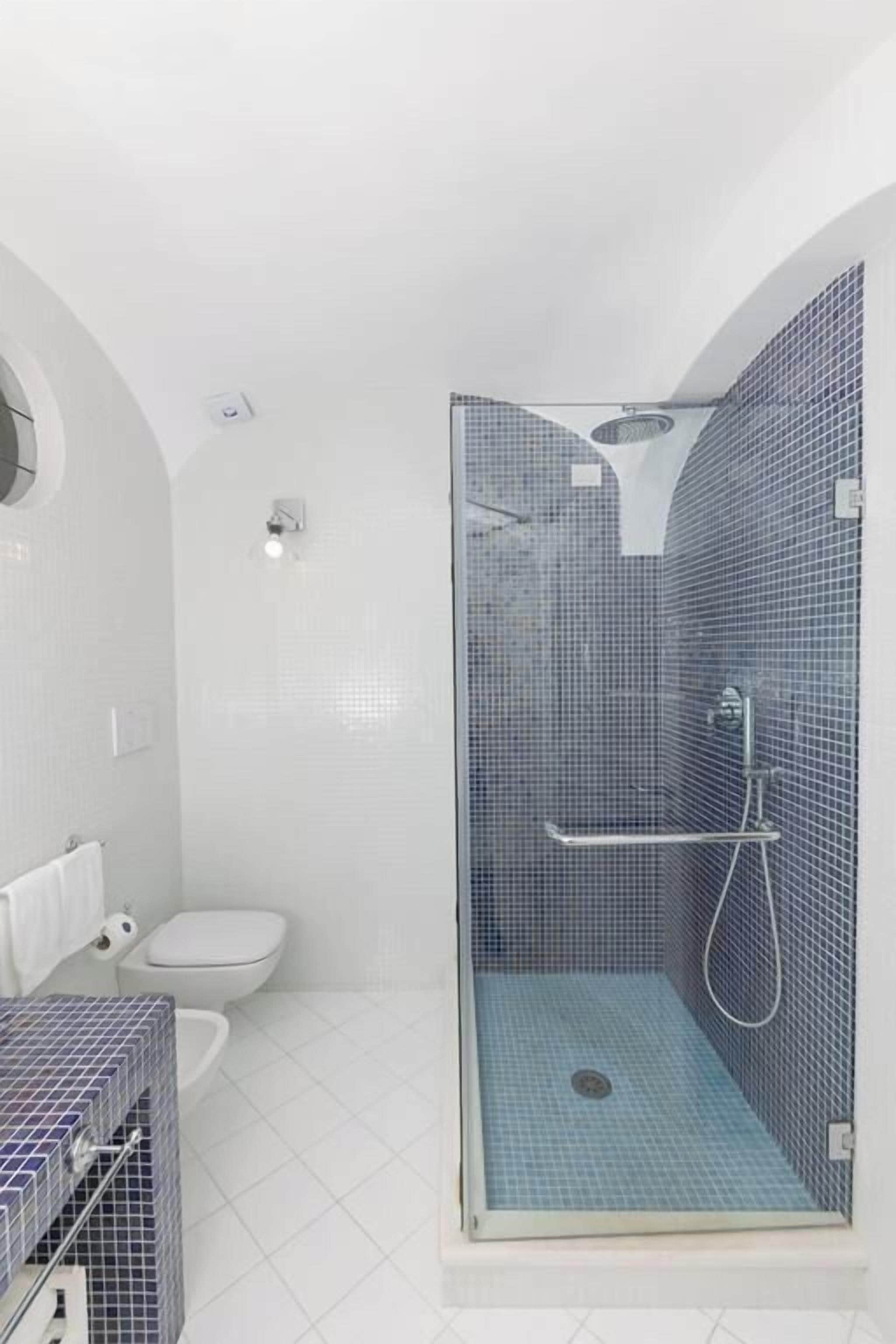 Une salle de bain moderne avec une douche à parois de verre, des murs recouverts de carreaux blancs et des toilettes blanches.