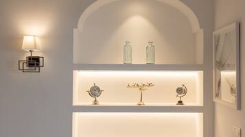 A wall with a modern light fixture, two glass bottles, and two wall-mounted clocks.