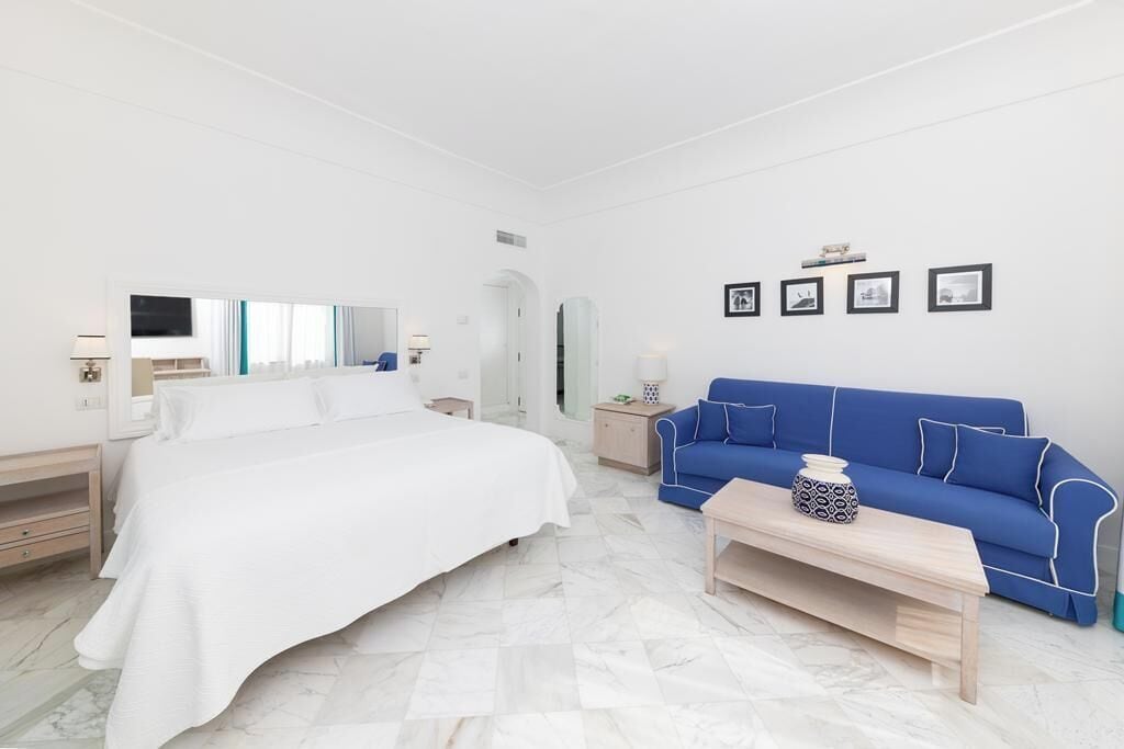Una habitación de hotel moderna con una cama grande, un sofá azul, una mesa de centro de madera y un televisor.