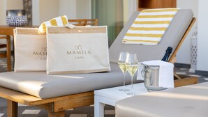 Un salón luminoso con una silla acolchada, una mesita con una jarra metálica y vasos, y dos bolsas de compras con el nombre de una marca.
