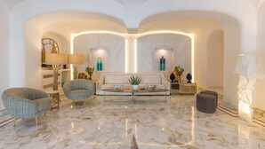 Un salón amplio con suelo de mármol, un sofá, dos sillones, una mesita de centro y una lámpara.