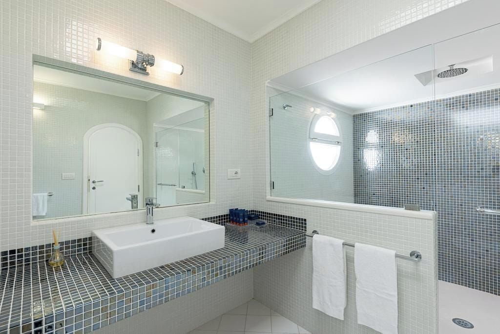 A modern bathroom with a large mirror, a white sink, and a shower area.