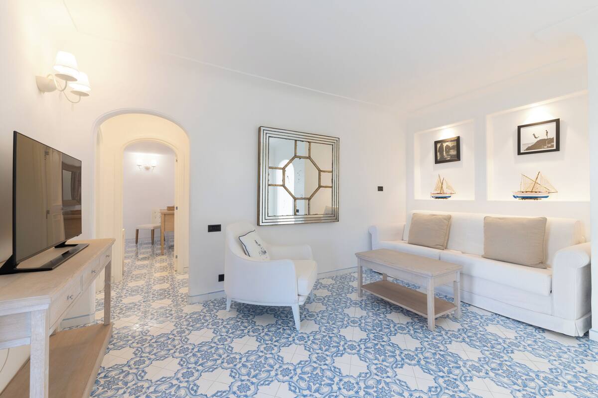 Una sala de estar moderna con televisor, mobiliario blanco, piso estampado y obras de arte en las paredes.