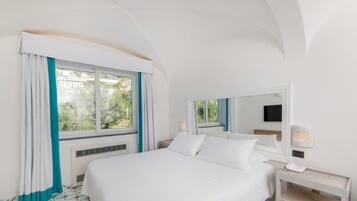 A hotel room with a large bed, a bedside table with a lamp, a window with curtains, and a wall-mounted TV.