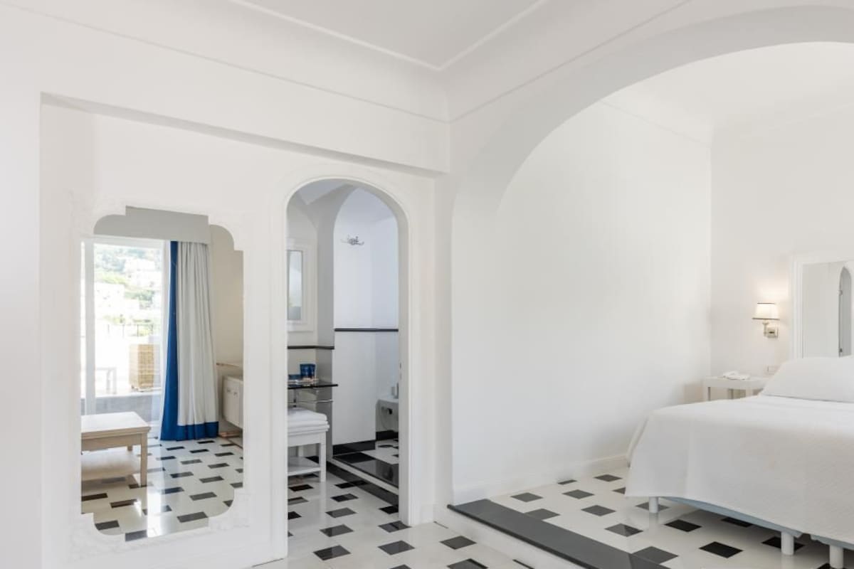 A hotel room with a bed, a desk, a chair, and a bathroom visible through an archway.