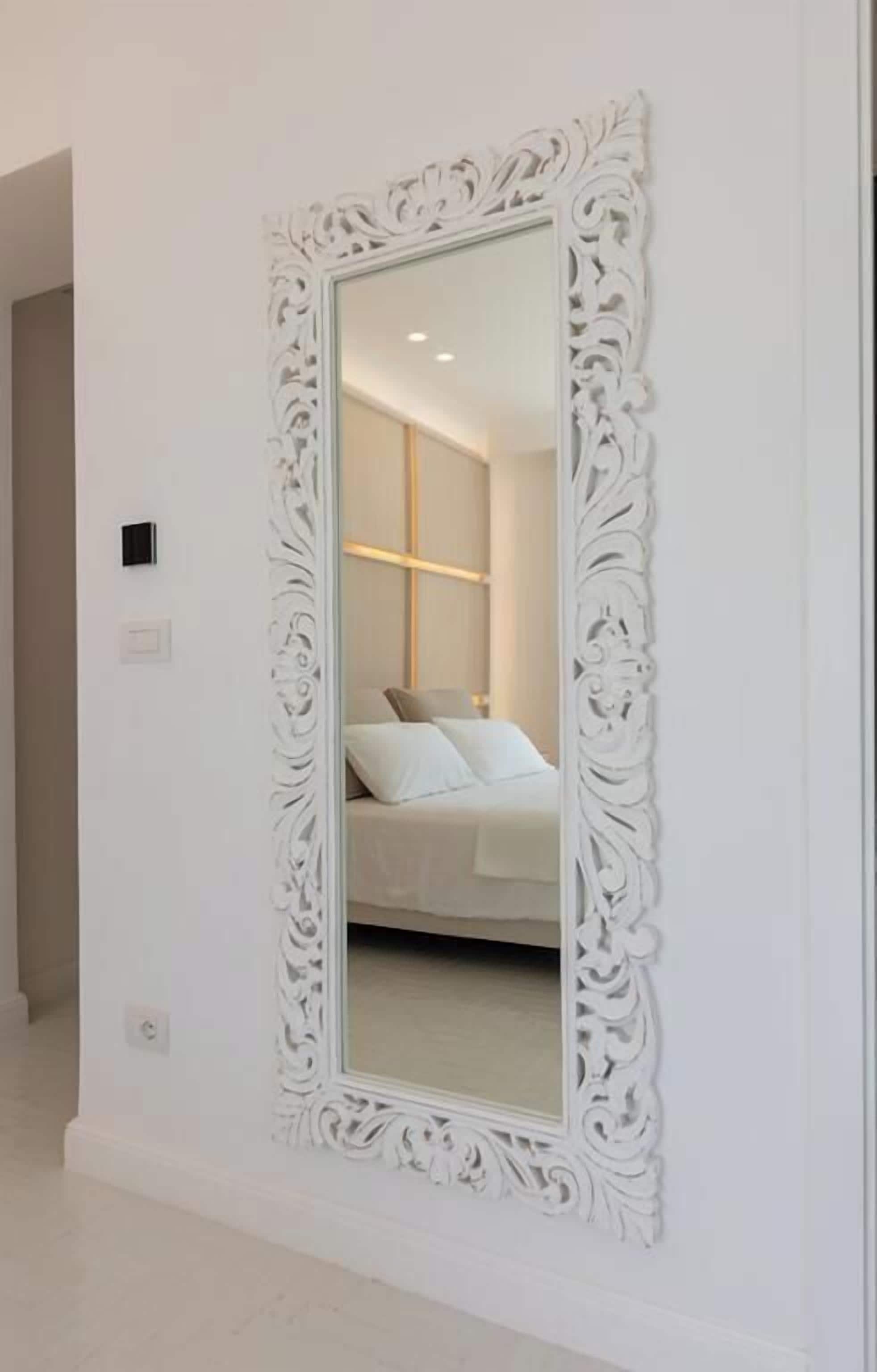 Un espejo grande y ornamentado con marco blanco sobre una pared blanca.