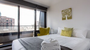 A hotel room with a bed, a chair, a window with a city view, and a wall art piece. - ABC Accommodation - 534 Flinders (Melbourne)