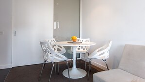 A modern dining area with a white table and chairs, a fruit bowl on the table, and a sliding door in the background. - ABC Accommodation - 534 Flinders (Melbourne)