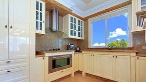 A kitchen with white cabinetry, a stainless steel oven, and a window with a view of trees. - ABC Accommodation - Rosebud (Rosebud)