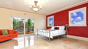 A hotel room with a bed, a red wall, a chandelier, and a view of palm trees through a sliding glass door. - ABC Accommodation - Rosebud (Rosebud)