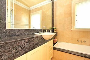Une salle de bain avec un comptoir en granit, un lavabo blanc, un miroir et une baignoire.