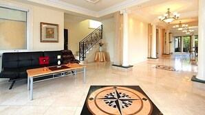 A spacious lobby with a black leather sofa, a wooden coffee table, and a large compass rug. A staircase with a railing leads to another area. - ABC Accommodation - Rosebud (Rosebud)