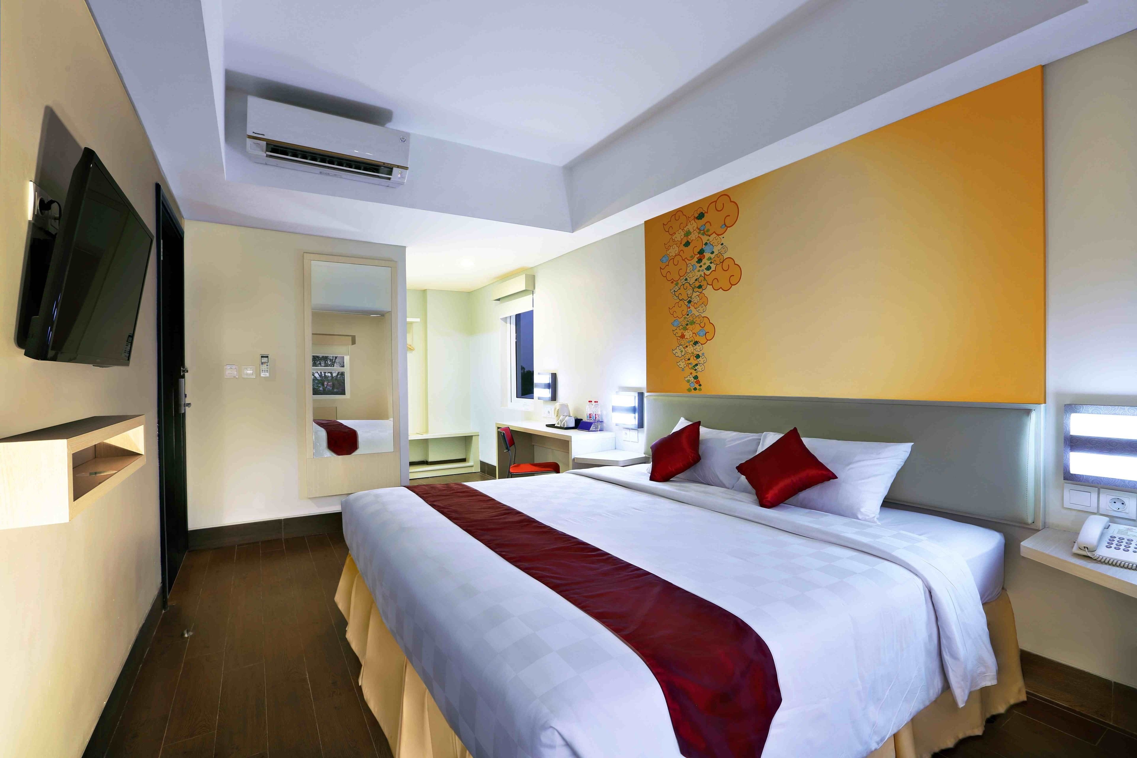 Habitación de hotel con una cama grande, un escritorio, una silla, un televisor y un baño visible a través de una puerta abierta.