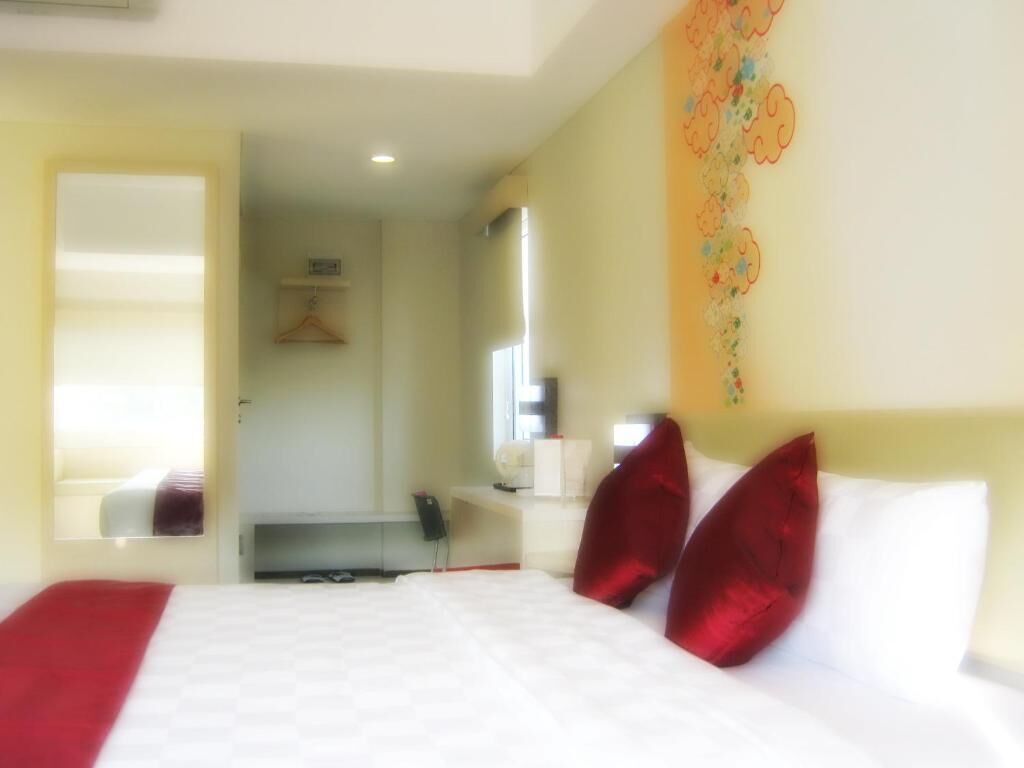 A hotel room with a bed, a mirror, a bedside table, and a wall with a floral pattern.