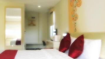A hotel room with a bed, a mirror, a bedside table, and a wall with a floral pattern.