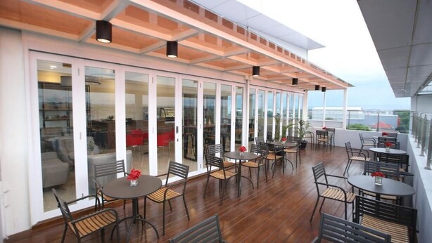 An outdoor patio area with tables and chairs, large glass doors leading to an interior space, and a view of the cityscape.