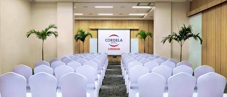 A conference room with rows of white chairs, a podium, and a screen displaying 'CORDELA HOTEL CIREBON'.